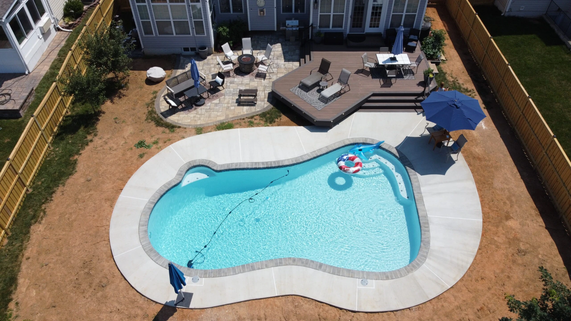 Aerial view of the custom deck and a pool that have beach lounge with a long wooden fence beside the house