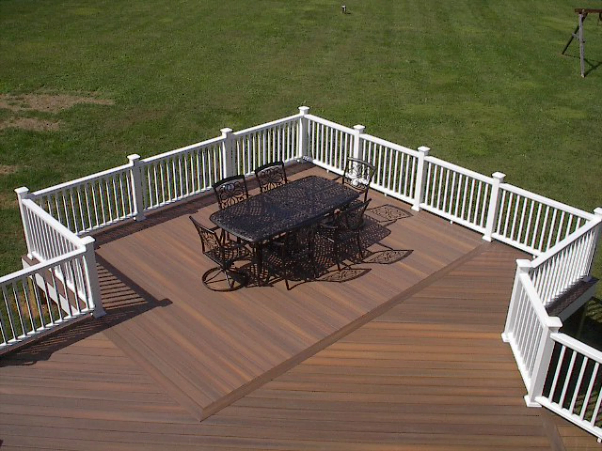 Hard wood deck with white railing and black table and chair with great view of lawn