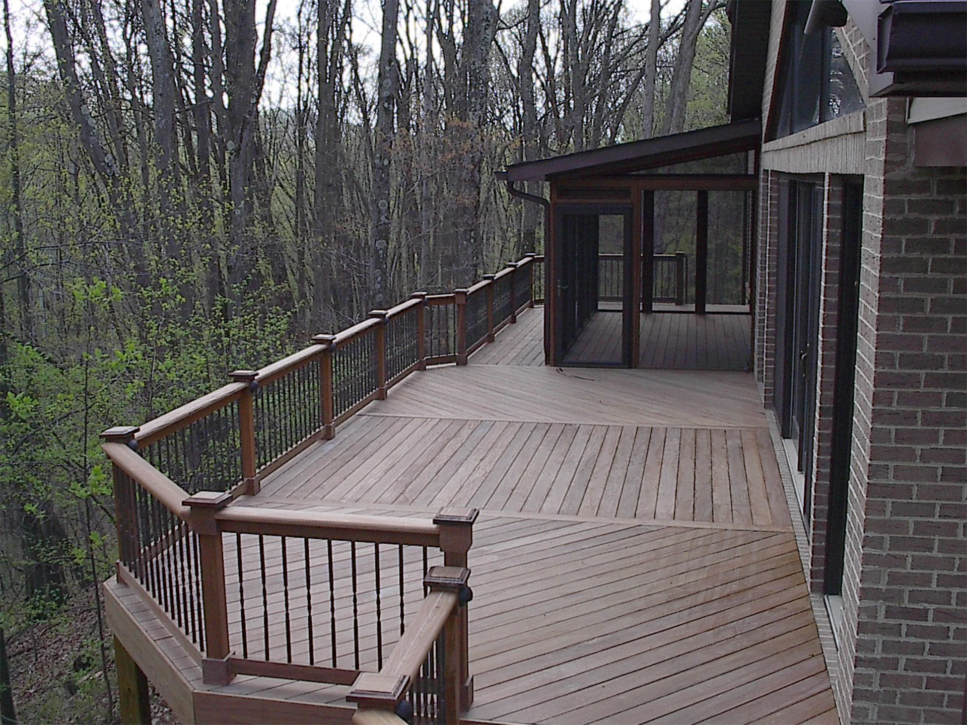 Ipa deck and screen porch with wooden railing and big trees on the back