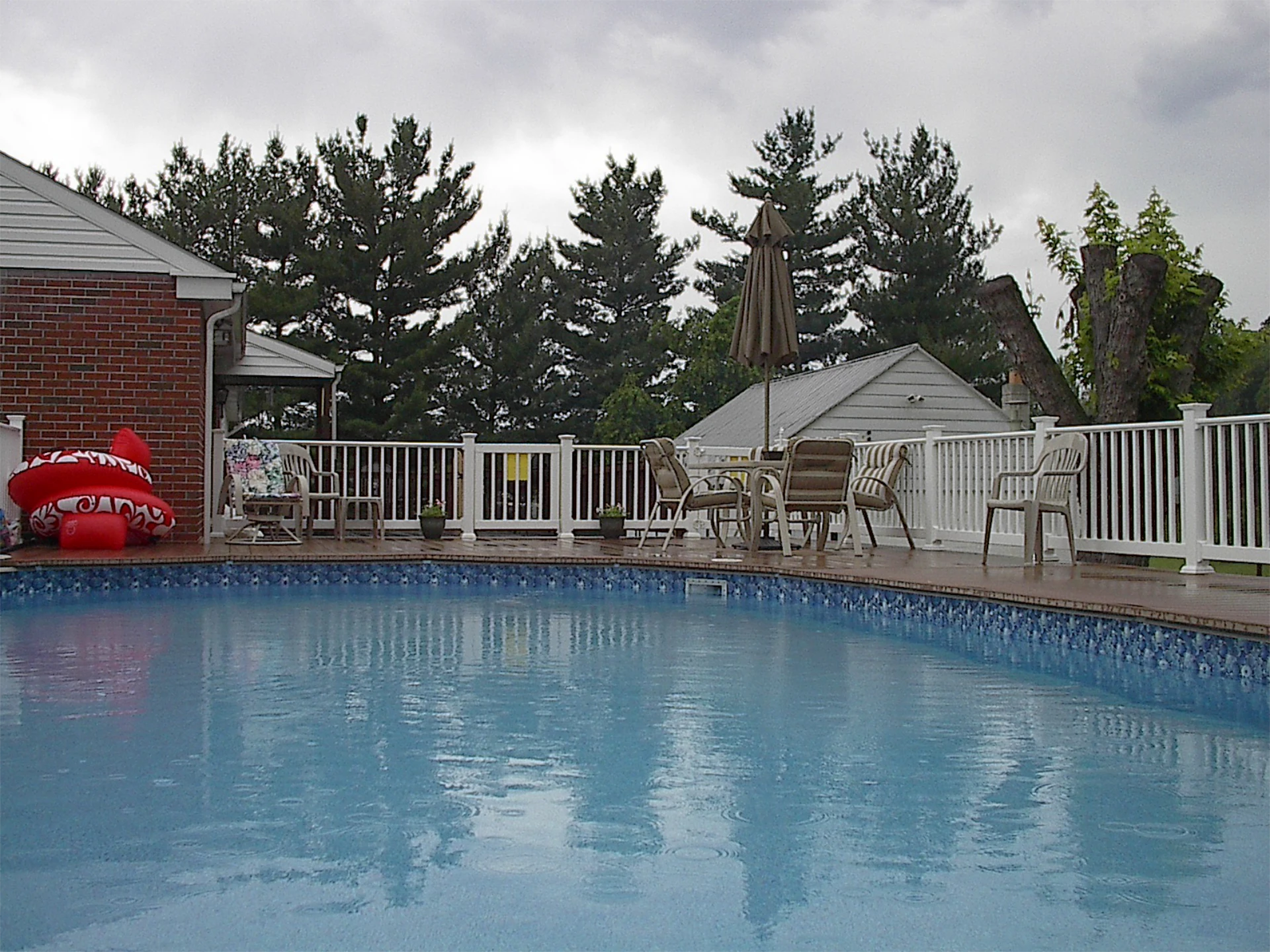 Wide pool with outdoor living furniture and long white fence with small gate